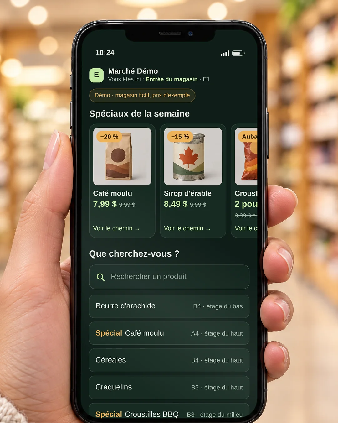 Téléphone tenu en main dans l’épicerie : l’écran affiche les spéciaux de la semaine et une recherche avec loupe.
